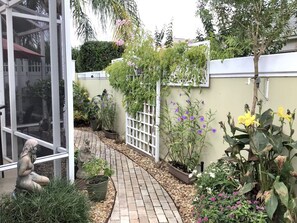 Un jardin avec un chemin dallé, des plantes en pot et une statue.