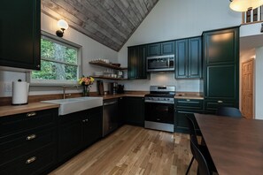 A modern kitchen with dark green cabinets, stainless steel appliances, a wooden countertop, and a window with a view of greenery. - Star View Cabin HOT TUB*Pets Ok*Long Range Views*K K Q 4TB (Deep Gap)