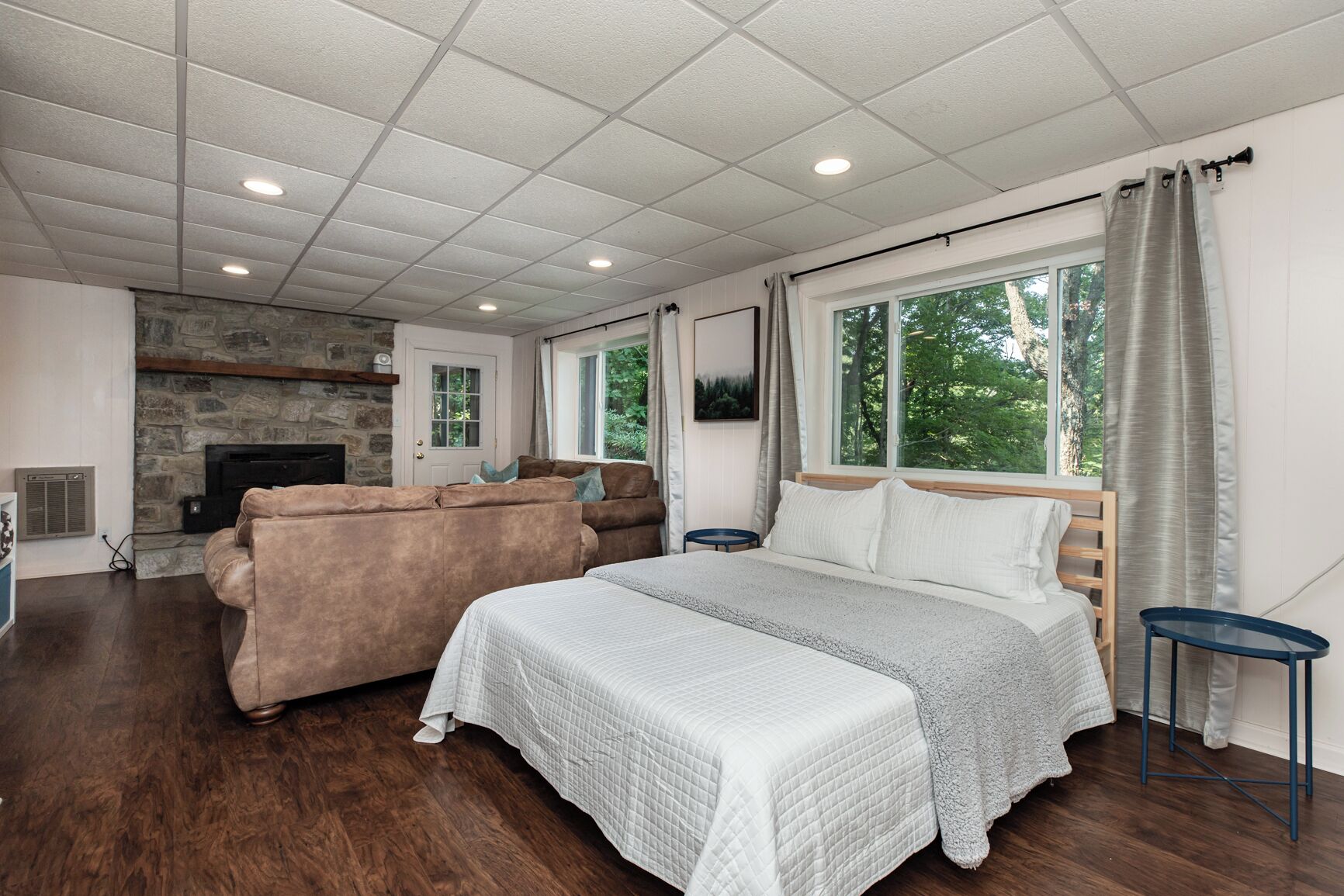 A bedroom with a large bed, a stone fireplace, a sofa, and a window with curtains.