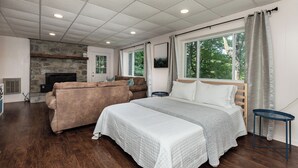 Une chambre avec un grand lit, une cheminée en pierre, un canapé et une fenêtre avec des rideaux.