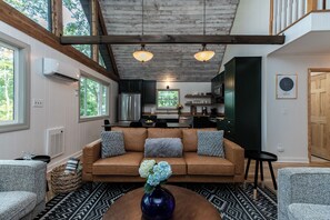 A cozy living room with a brown sofa, two armchairs, and a coffee table with a vase. A kitchen is visible in the background with modern appliances. - Star View Cabin HOT TUB*Pets Ok*Long Range Views*K K Q 4TB (Deep Gap)