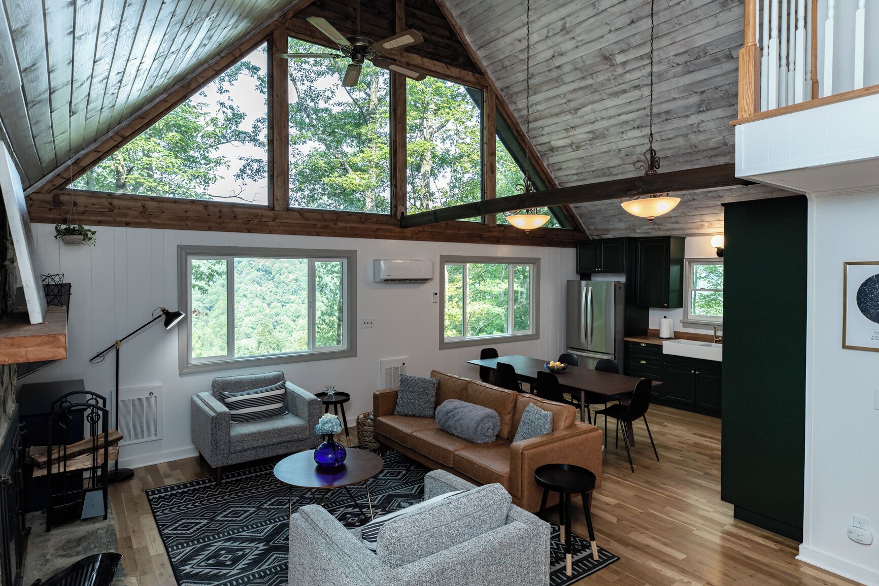 A spacious living area with a high ceiling, large windows, and a modern kitchen.