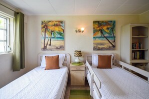 A room with two beds, a nightstand with a lamp, a bookshelf, and two wall paintings of palm trees. - 3 min walk from the beach - Bella Figura (Apt 3) (Hastings)