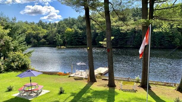 A lakeside deck with a flag, a table with an umbrella, and a small tree. - Waterfront cottage with great view  (parry sound)