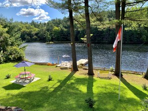 A lakeside deck with a flag, a table with an umbrella, and a small tree. - Waterfront cottage with great view (parry sound)