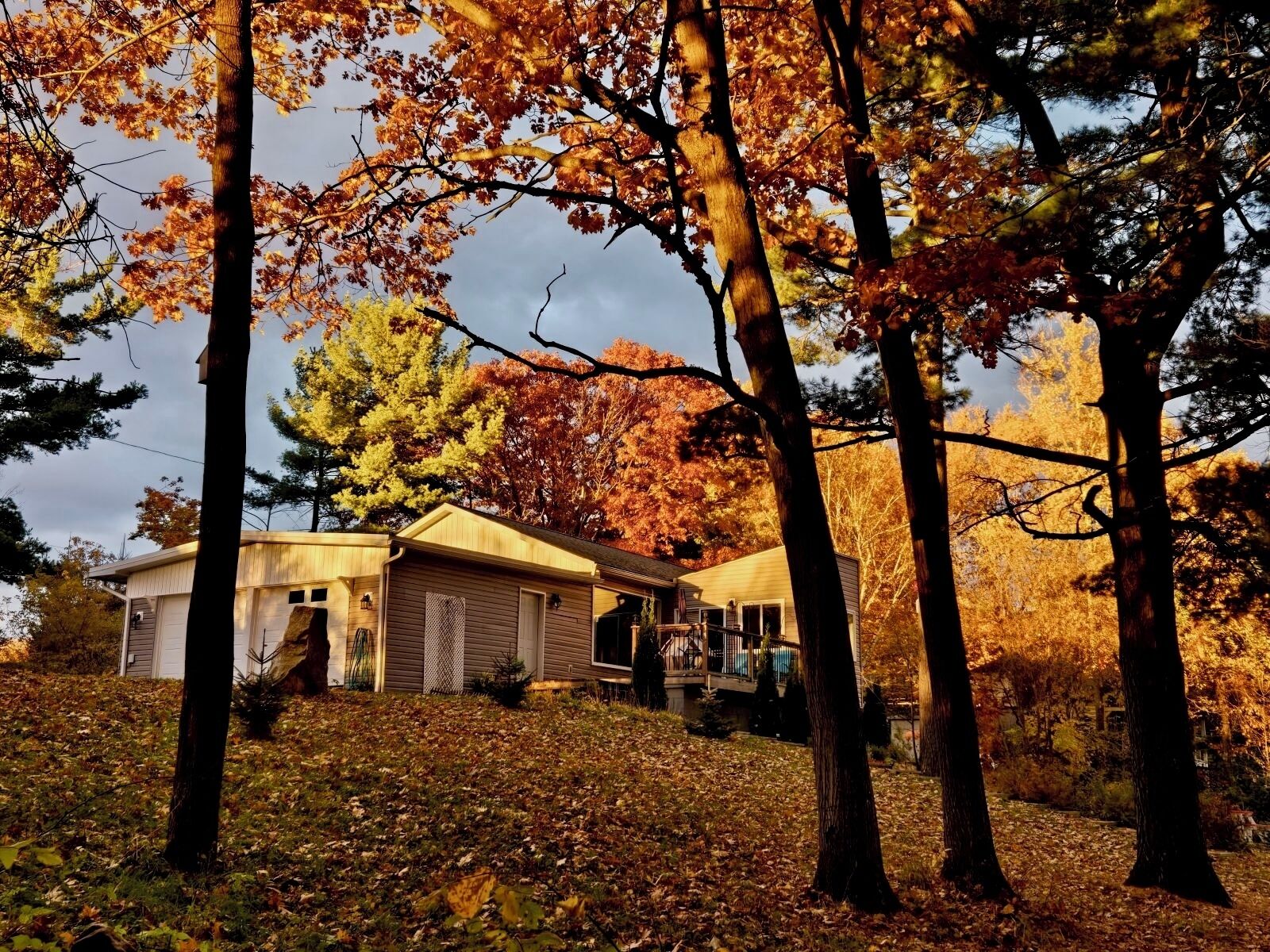 Une maison à deux étages dotée d’un porche abrité et d’un garage, entourée d’arbres aux feuilles d’automne.