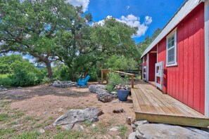 A red wooden building with a wooden deck, surrounded by trees and rocks. - Sunflower Ridge Bungalow - An Outdoor Enthusiasts Wonder (San Marcos)