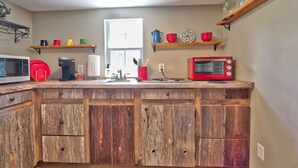 Una cucina con mobili in legno, un forno a microonde, un tostapane rosso ed scaffali con stoviglie e utensili.