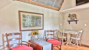 Zona pranzo con sedie di legno e un tavolo, un'opera d'arte incorniciata al muro e uno scaffale con oggetti decorativi.