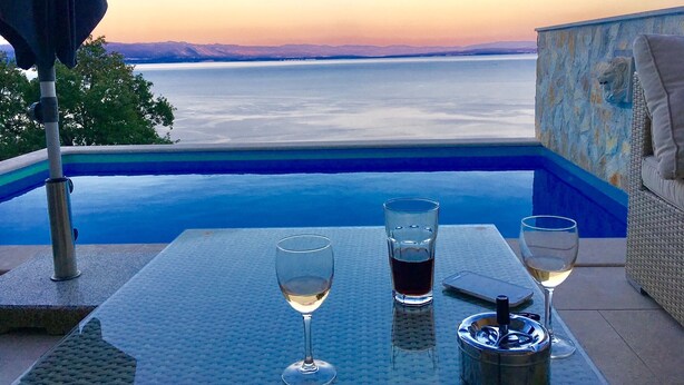 A table with two wine glasses and a tumbler, overlooking a pool and a scenic view of mountains and water at sunset. - Villa Sabine Medveja Cres. Studio-appartement mit Wlan und Pool (Medveja)
