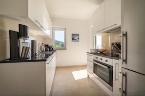 A modern kitchen with stainless steel appliances, white cabinetry, and a view of the outdoors through a window.