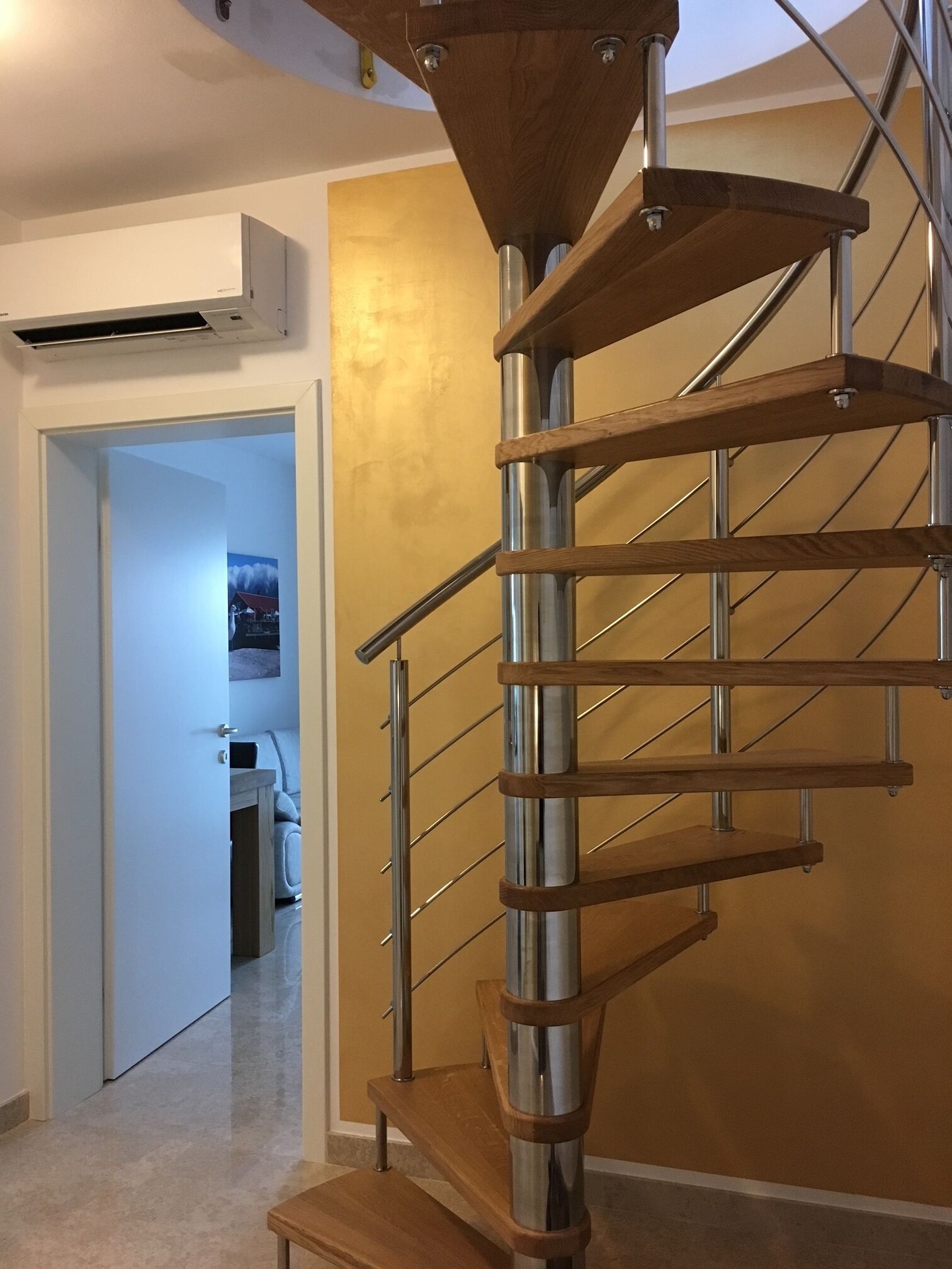 En modern spiraltrappa med trästeg och metallräcken, som leder upp till ett övre våningsplan.