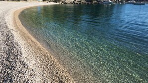 A pebble beach with clear water, boats, and trees in the background. - Villa Sabine Medveja Cres. Studio-appartement mit Wlan und Pool (Medveja)