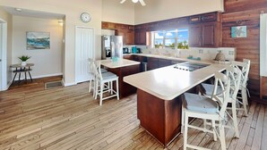 A modern kitchen with wooden cabinets, a central island, and a dining area with white chairs. - Dreamview by Distinctive Beach Rentals (St. Augustine)
