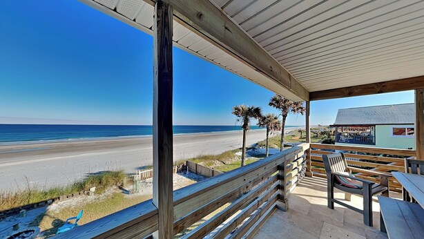 A beachside patio with wooden railings, a seating area, and a view of the beach and ocean. - Dreamview by Distinctive Beach Rentals (St. Augustine)
