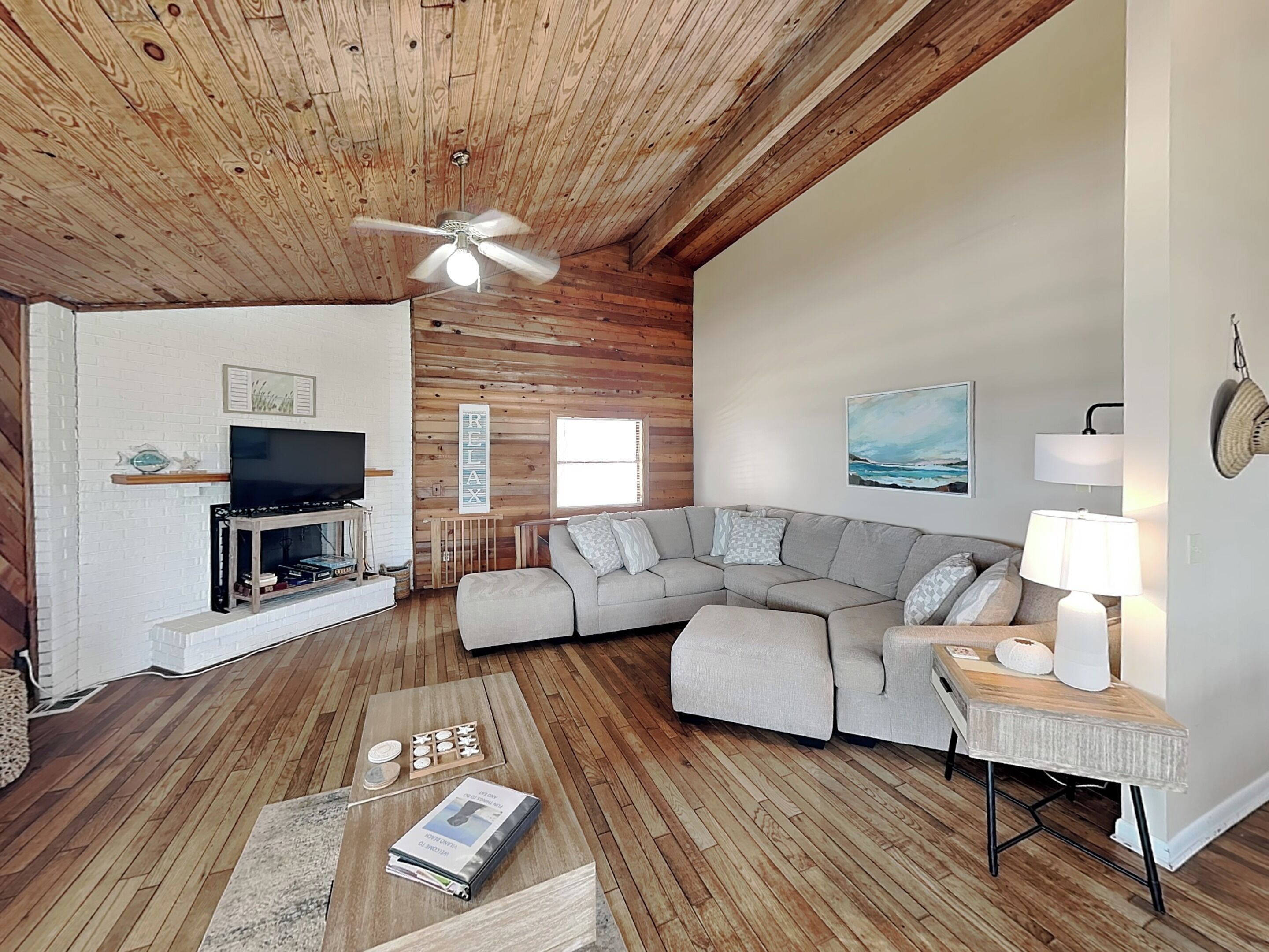 A cozy living room with a wooden ceiling, a sectional sofa, a television, and a coffee table.
