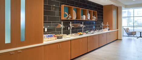 Una cocina moderna con armarios de madera, salpicadero negro y una encimera amplia con diversos objetos.