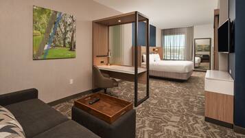 A hotel room with a large bed, a desk, a chair, a TV, and a painting on the wall.
