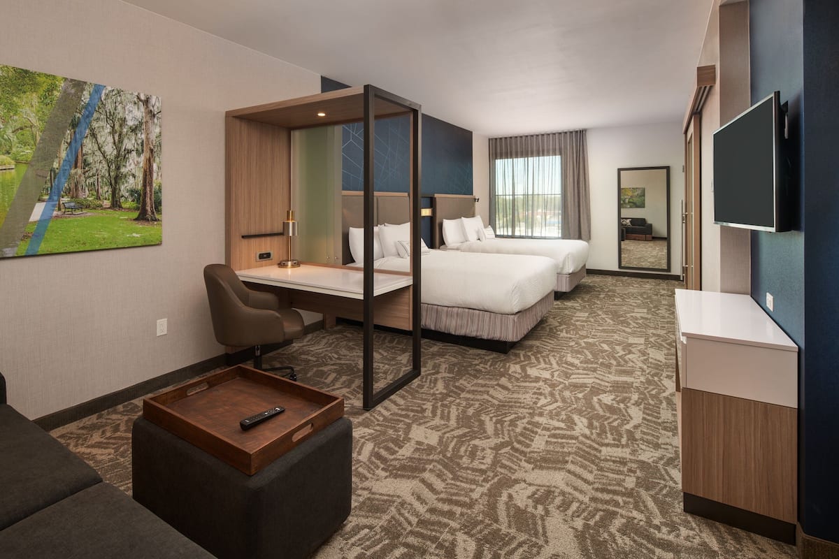 A hotel room with two beds, a desk, a chair, a TV, and a painting on the wall.