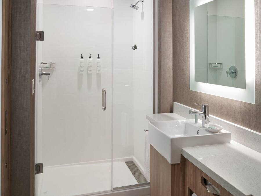 Een moderne badkamer met een douchecabine van glas, een witte wastafel en een grote spiegel.
