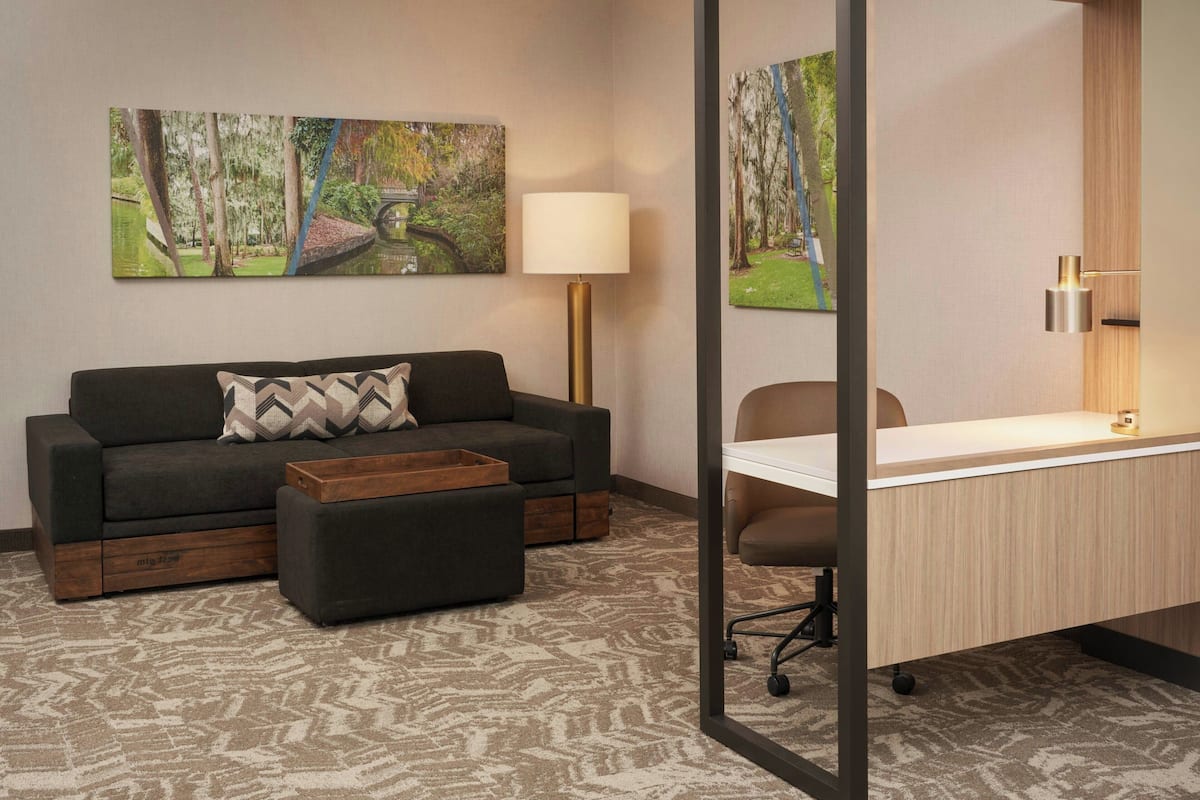 A modern room with a dark grey sofa, a wooden coffee table, a desk with a chair, and two wall-mounted lamps.