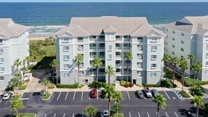 Un hôtel à plusieurs étages doté d’un parking et bordé de palmiers, offrant une vue sur une plage et l’océan.