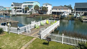 A waterfront property with a dock, a white picket fence, and a grassy area. - Canal home, 3 bedrooms, 2 bathrooms, dock, pet friendly, fenced in back yard. (Supply)