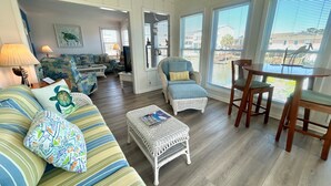 A spacious living area with a sofa, armchair, and dining table, featuring a view through large windows. - Canal home, 3 bedrooms, 2 bathrooms, dock, pet friendly, fenced in back yard. (Supply)