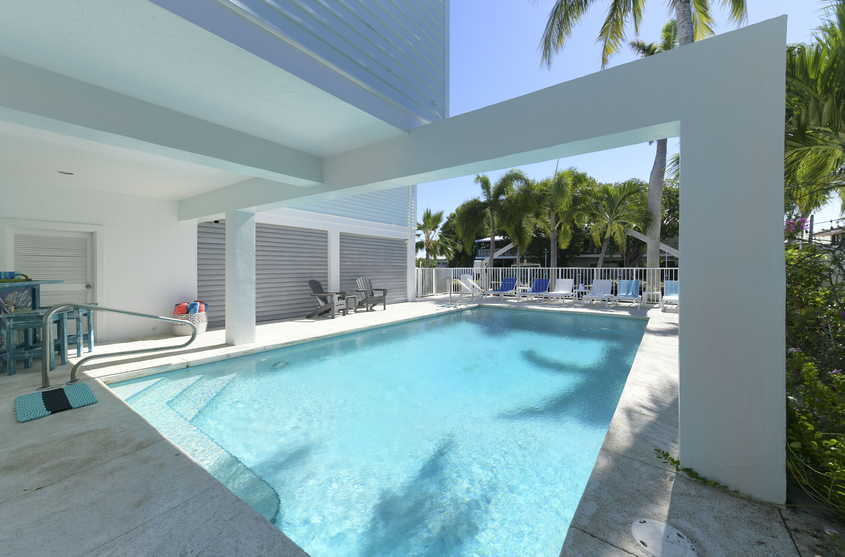 Une piscine à l’eau d’un bleu cristallin, entourée d’une terrasse blanche et de chaises longues.