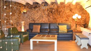 A cozy living room with a stone wall, a leather sofa, green armchairs, and a coffee table. - Casa Rustíca Cal Mian (Almoster)