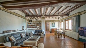 A spacious living room with a fireplace, a dining area, and a bookshelf filled with books. - Casa Rustíca Cal Mian (Almoster)