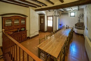 A spacious dining area with a long wooden table and chairs, a wooden cabinet with glass doors, and a staircase leading to an upper level. - Casa Rustíca Cal Mian (Almoster)