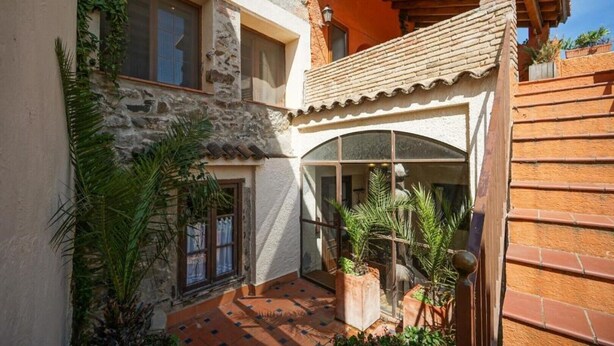 A courtyard with a stone wall, a wooden pergola, and potted plants. - Casa Rustíca Cal Mian (Almoster)