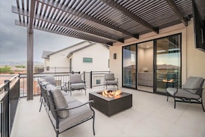 Une terrasse extérieure couverte, dotée d’un foyer, de sièges et offrant une vue sur un bâtiment moderne.