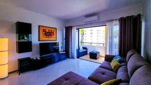 A modern living room with a large flat-screen TV, a sofa set, a coffee table, and a balcony with a view of buildings. - FLH Vilamoura Balcony with Pool (Vilamoura)