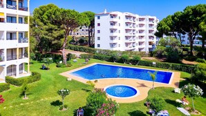 A pool area with a rectangular pool and a circular hot tub, surrounded by well-maintained lawns and trees. - FLH Vilamoura Balcony with Pool (Vilamoura)