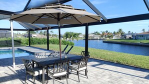 A covered patio with a table and chairs, overlooking a body of water and a residential area. -  Private enclosed heated pool with Gulf access. Panoramic Lenai (Cape Coral)