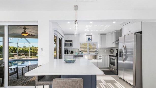 A modern kitchen with a central island, stainless steel appliances, and a view of a swimming pool. -  Private enclosed heated pool with Gulf access. Panoramic Lenai (Cape Coral)