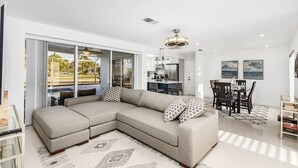 A modern living room with a sectional sofa, a dining area with a table and chairs, and a kitchen in the background. -  Private enclosed heated pool with Gulf access. Panoramic Lenai (Cape Coral)