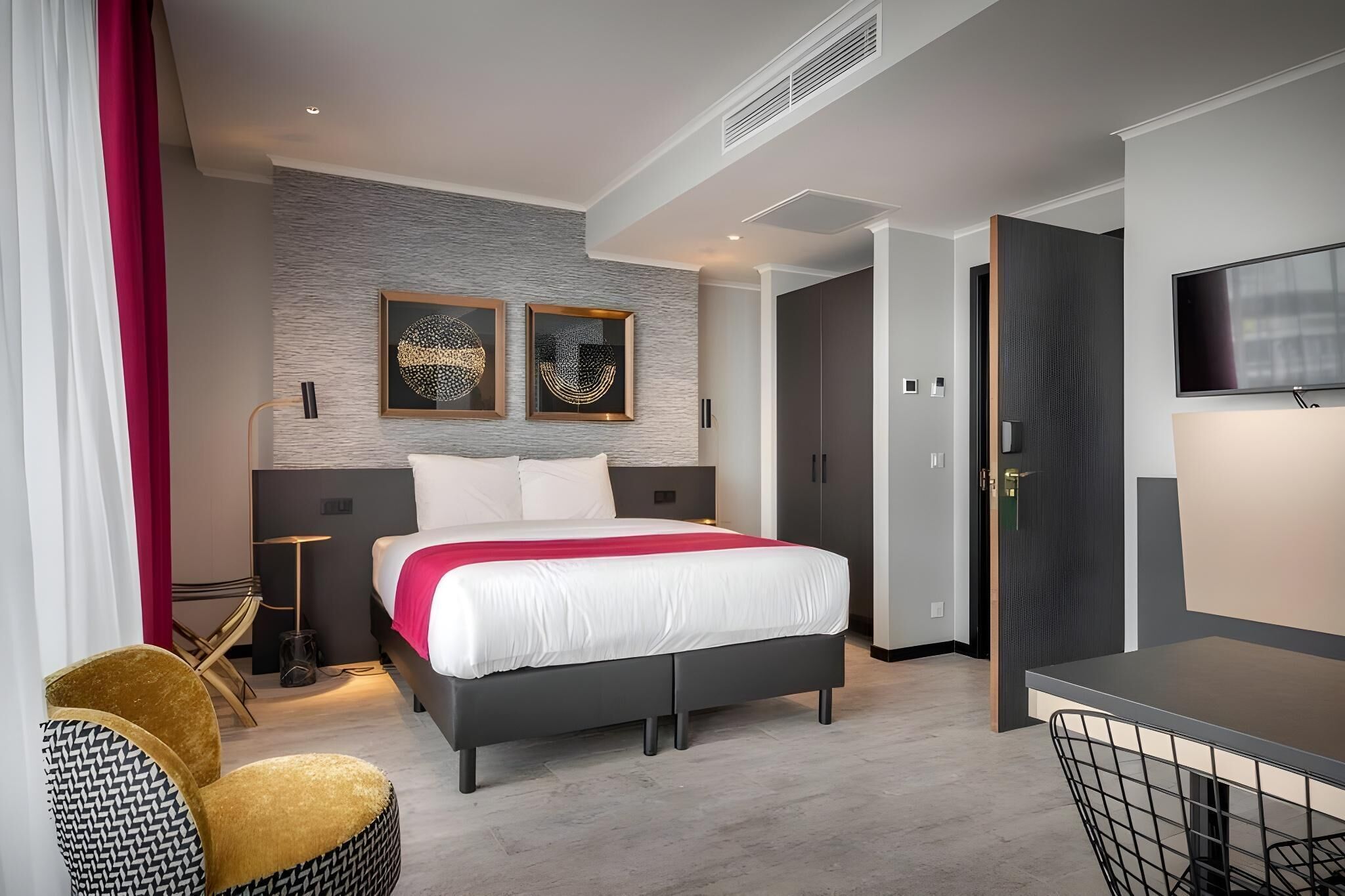 Quarto de hotel moderno com uma cama, uma escrivaninha, uma cadeira e obras de arte na parede.