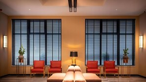 A modern hotel lobby with a central seating area, two large windows with blinds, and potted plants. - Amory Hotel (Antwerp)