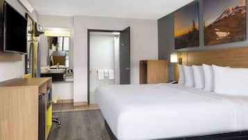 A hotel room with a bed, a desk, a television, a bathroom, and artwork on the walls.