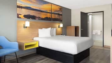 Habitació d'hotel moderna amb un llit gran, una tauleta de nit, un escriptori, una cadira i un quadre d'un capvespre sobre un llac.