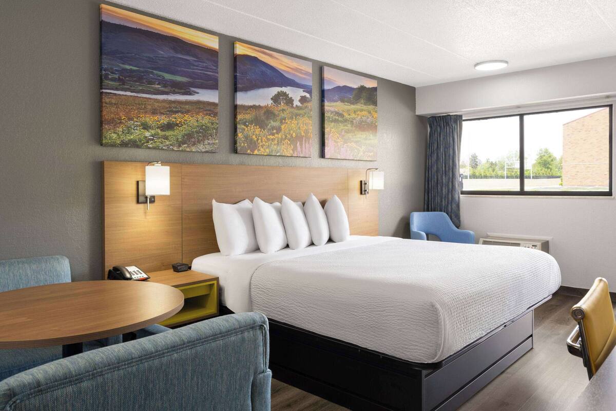 A hotel room with a large bed, a desk with a lamp, a chair, and a window with curtains.
