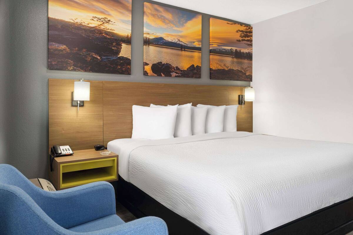 A hotel room with a large bed, a wooden headboard, two wall-mounted lamps, a bedside table with a phone, and a blue armchair.