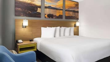 A hotel room with a large bed, a wooden headboard, two wall-mounted lamps, a bedside table with a phone, and a blue armchair.