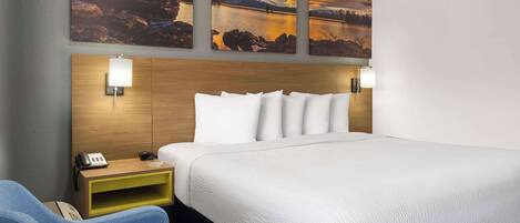 A hotel room with a large bed, a wooden headboard, two wall-mounted lamps, a bedside table with a phone, and a blue armchair.