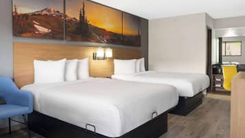 A hotel room with two beds, a blue chair, a wooden headboard, and a large landscape painting above the beds.