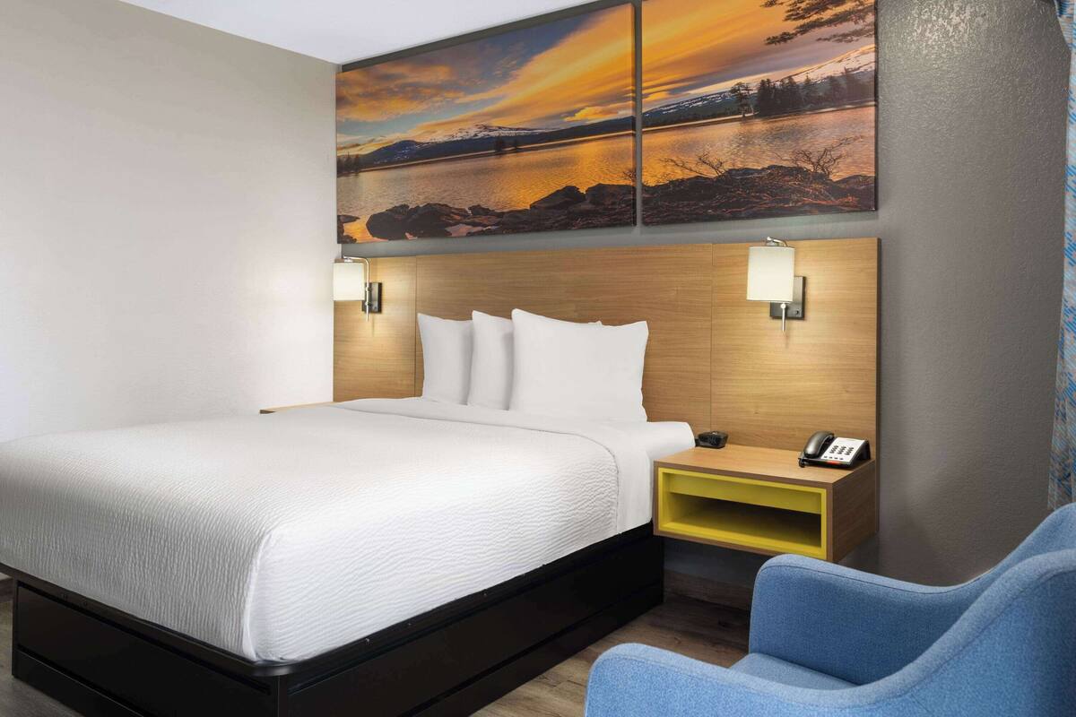 A modern hotel room with a large bed, a bedside table with a phone, and a wall-mounted light.