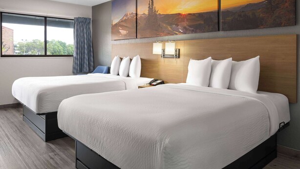 A hotel room with two beds, a large window with a view, and a painting above the beds. - Days Inn by Wyndham Columbus/Worthington (Columbus)